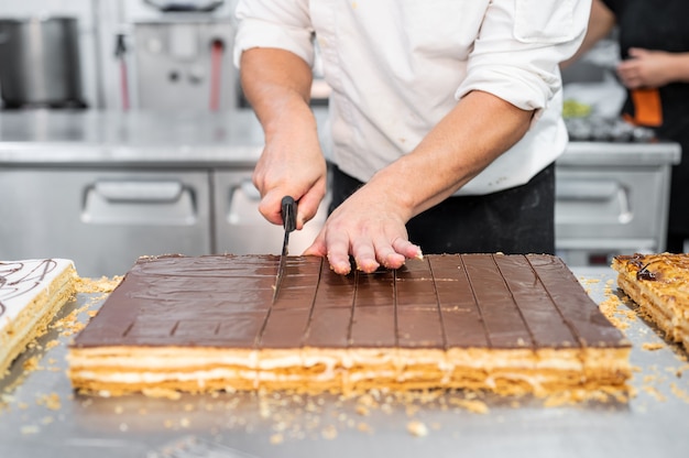 Close up of a pastry chef cutting a large cake in portions