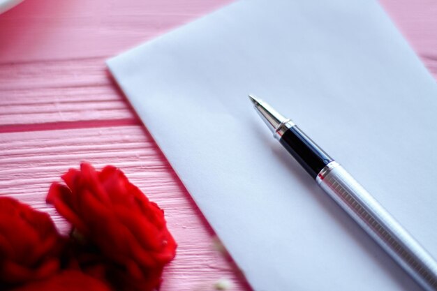 Photo close up pen on white blank paper and red flowers