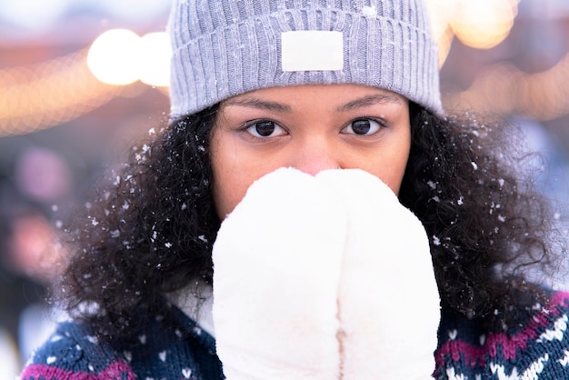 Close-up, pensive African American girl on a walk in winter. The portrait froze, young. A dark-skinned black woman in the park warms her hands in mittens.