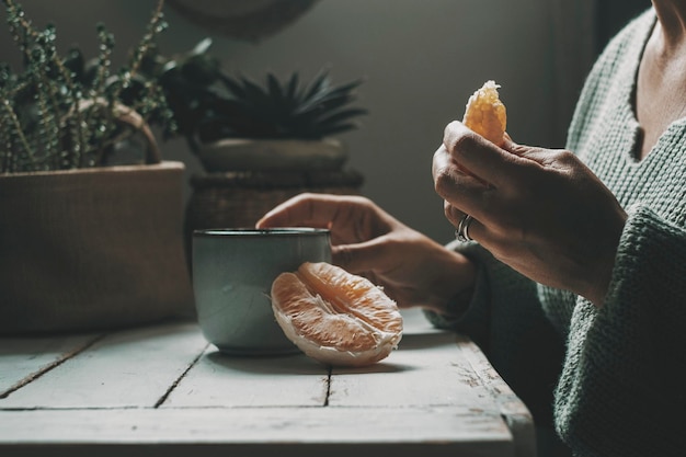 Close up of people in healthy eating concept lifestyle Hands of a woman with orange fruit and herbal tea for diet of health purpose Relax leisure activity at home with light breakfast Vitamins