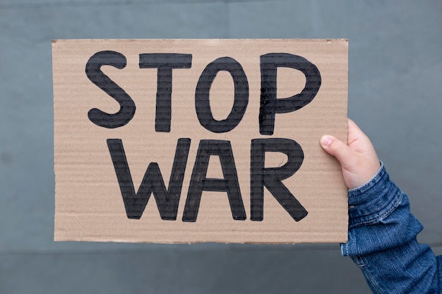 Close up of persons hand holding handmade banner with Stop War slogan isolated on grey background