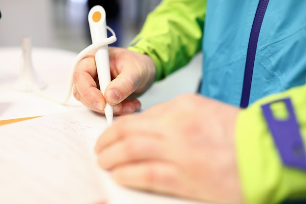 Close-up of persons hand signing check or receipt with white pen. Man in bright jacket. Male in bank filling important form on paper. Money and accountability concept