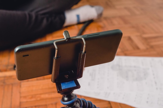 Close up phone on a tripod front of an unrecognizable person sitting on the floor