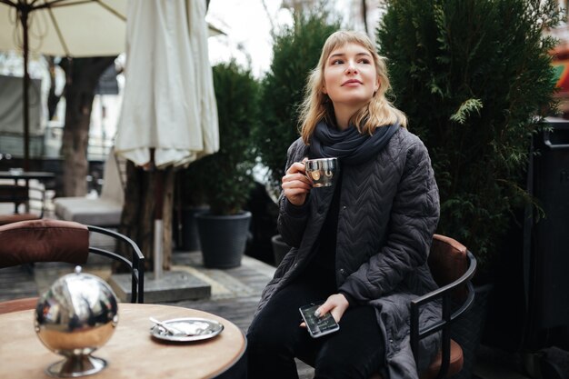 Photo close up photo of beautiful lady sitting at the table on street and drinking coffee