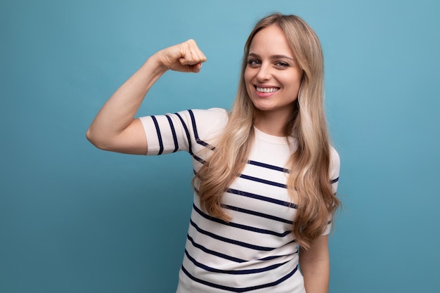 Close up photo of champion strong girl in casual wear showing biceps on blue isolated background