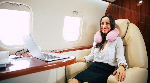 Close-up photo of a charming lady in a white blouse, who is taking a nap in her window seat on business class aircraft.