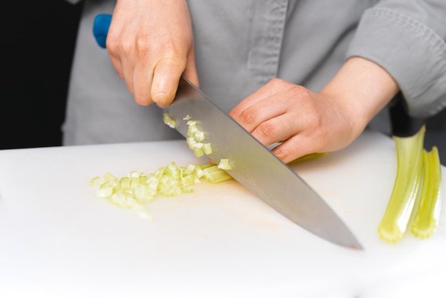 Close up photo of female chef cutting celery with knife on white board