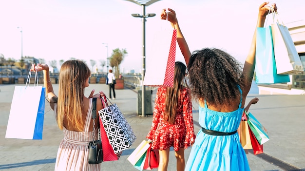 Close up photo of four girls walking along the city streets carrying shopping bags with their backs to the camera