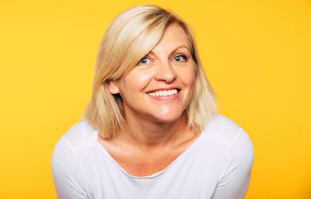 Photo close up photo of happy smiling beautiful cute lovely blonde senior woman with beauty clean skin in casual wear isolated on yellow background