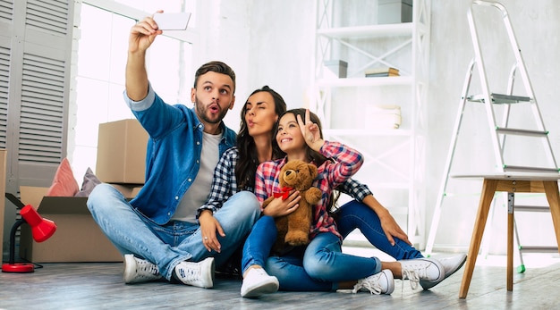 Close up photo, joyful family is taking selfie together in their new house in front of a pile of cardboard boxes