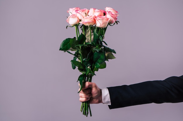 Close up photo of male hand holds the bouquet of roses. Celebration, holidays and gifts concepts. St Valentines dat. Lovers day