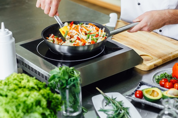 Close up photo, man hands with apron frying vegetables, modern kitchen