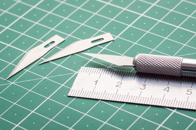 Photo close up photo of metal knife set of blades and ruler on cutting mat