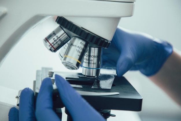 Close up photo of a microscope with a glass slide and hands of lab assistant touching it