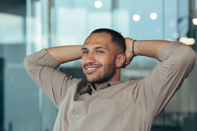 Close up photo of mixed race man relaxing in office with hands behind head looking out window and