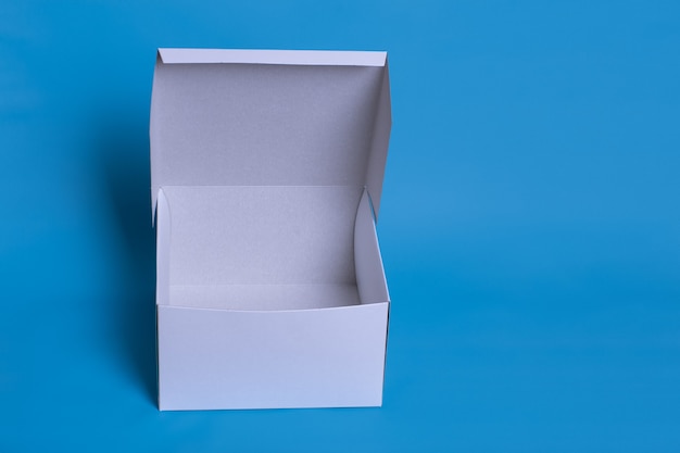 Close up photo of an open white box with shadow on a dark blue background. Clear simple template for packaging design.