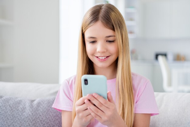 Close up photo of positive small kid girl study remote rest relax use smartphone follow share repost quarantine stay home information sit comfort couch in house indoors