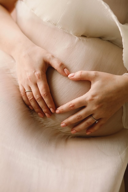 Photo close up photo of pregnant woman which makes heart shape with hands on her stomach