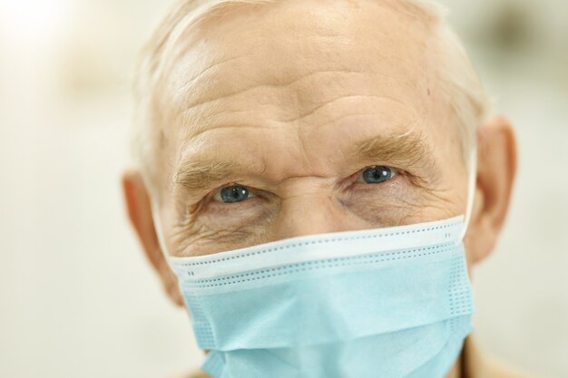 Close-up photo of senior citizen wearing surgical mask while looking at the camera