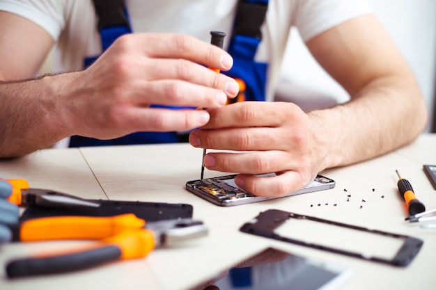 Close up photo of specialist man while he is repairing broken smartphone on his workplace with professional tools