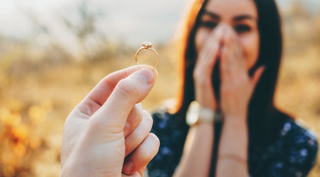 Close up photo of a wedding ring with diamond shown to the girl while she is amazed and covers her face with palms