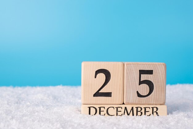 Close up photo of wooden cubes calendar showing the 25th of december standing in snow with space for text empty blank place