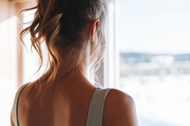 Close up photo of Young slender fitness blonde woman from back near window of home