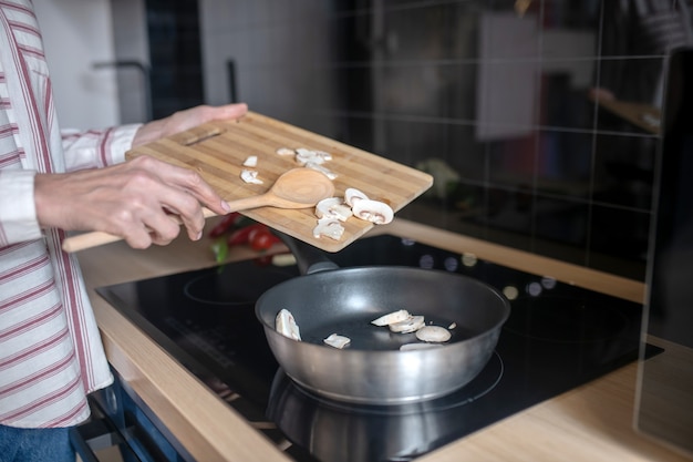 Close up picture of a woman putting veggies on a frying pan