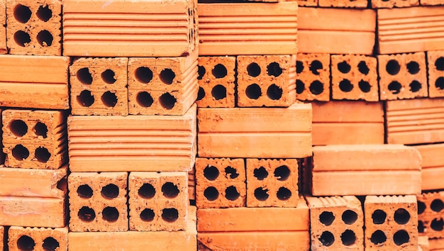 Close up pile new red brick with holes stacked in rows wall Store of bricks ready for building or sale Background Building Construction materials Texture outdoor storage or manufacturing concept