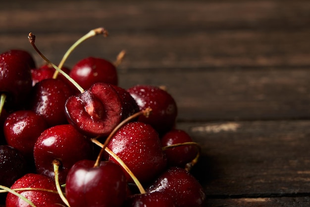 Close up of pile of sweet red cherries with stalks and leaves on a wooden table wooden background.