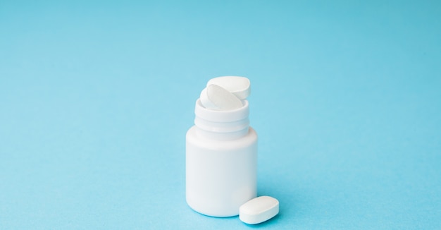 Close up pills spilling out of pill bottle on blue background