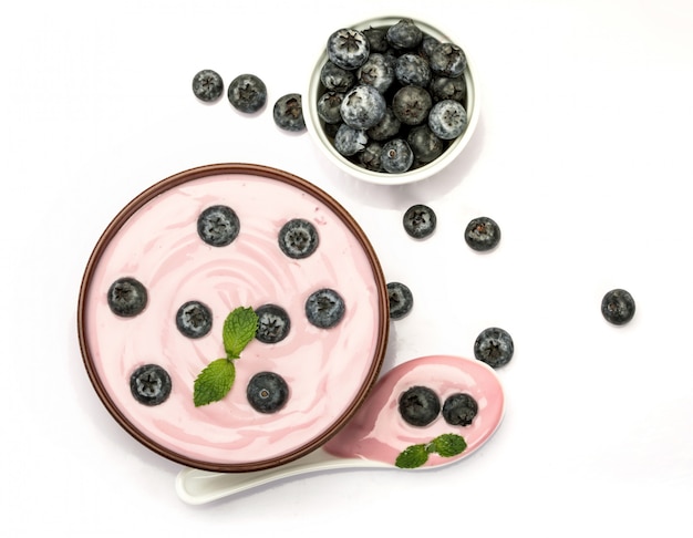 Close up pink creamy homemade blueberries fruit yogurt with fresh green mint leaf on white background.