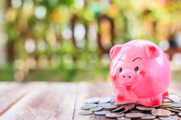 Close up pink piggy bank and coin pile on wooden plank. savings concept.