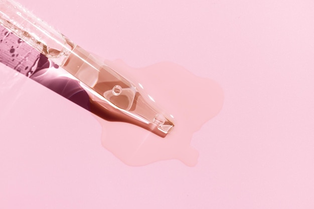 Close up of a pipette with pouring liquid serum on pink background Copy space