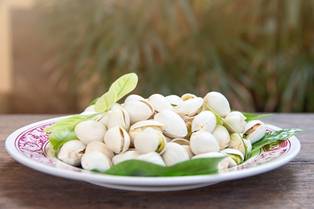 Close up of Pistachios nuts on wooden table. Pistachio in wooden bowl with green leaves