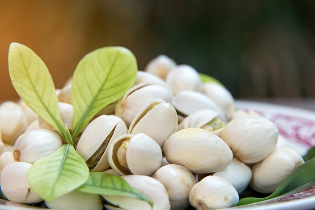 Close up of Pistachios nuts on wooden table. Pistachio in wooden bowl with green leaves