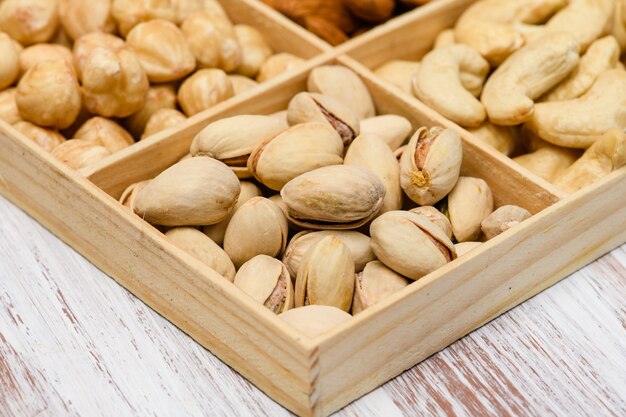 Close-up of pistachios in a wooden box. Assortment of nuts in the background.