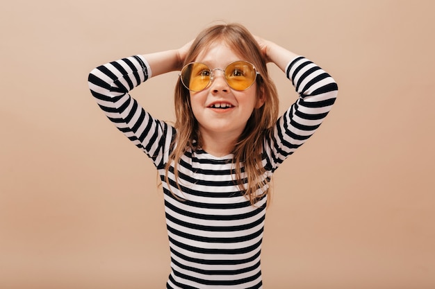 Close up portrait of adorable pretty girl in round trendy glasses and stripped dress holding up hands and smiling