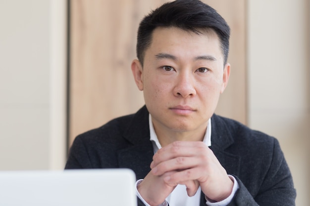 Close-up portrait asian pensive young office worker man at workplace. face a serious male business manager in formal suit thinking about solving a problem. Businessman at desk with computer or laptop