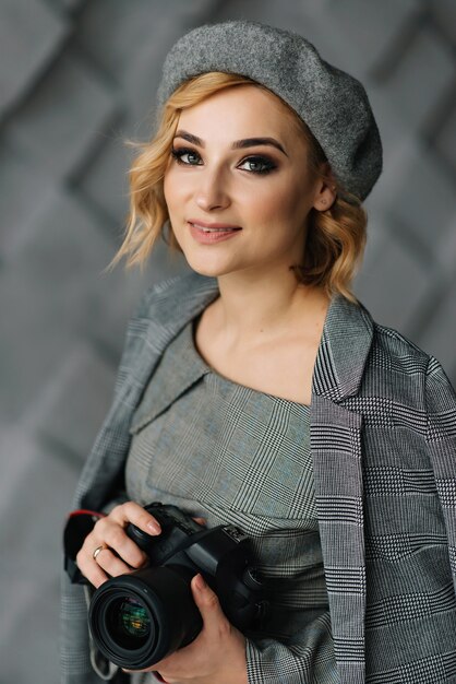 Close-up Portrait of an attractive girl photographer in stylish clothes and a beret with a camera in her hands with a smile. The concept of creative professions.