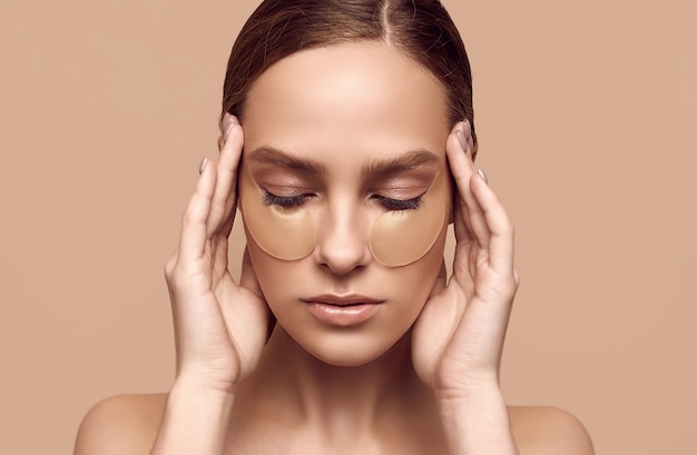 Close-up portrait of attractive sensual girl with naked shoulders applying patches on her face