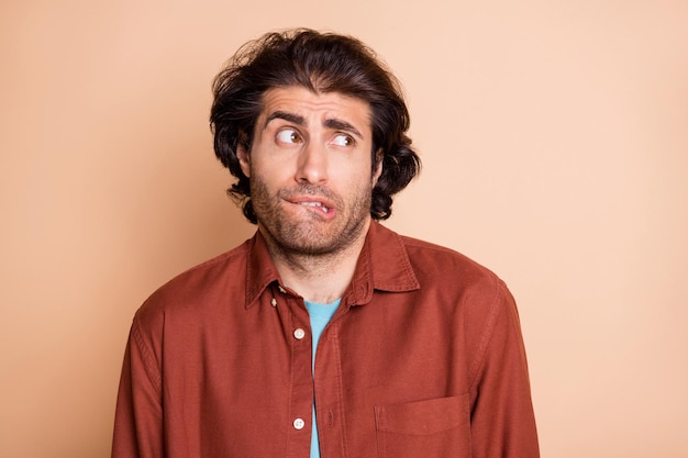 Close-up portrait of attractive worried guy biting lip looking aside isolated over beige pastel color background