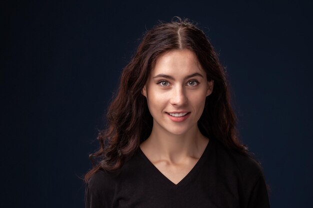 Close-up portrait of a beautiful brunette with curly hair and professional make-up posing on a black background.