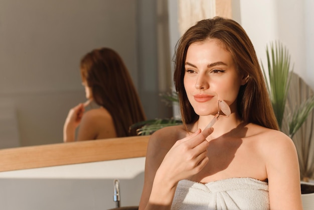 Close up portrait of beautiful brunette woman using jade roller massager for lymphatic drainage facial massage Skin care and rejuvenation