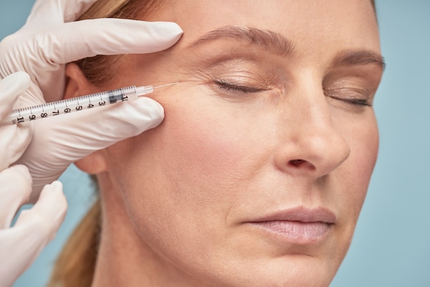 Close up portrait of a beautiful mature woman keeping eyes closed while receiving hyaluronic acid