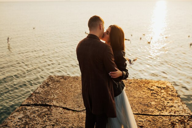 Close up portrait of a beautiful stylish young couple in love standing and kissing on the beach at sunset.