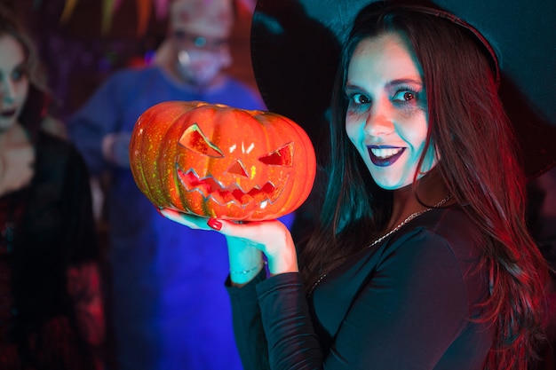 Photo close up portrait of beautiful woman dressed up like a witch for halloween holding a pumpkin. halloween event.