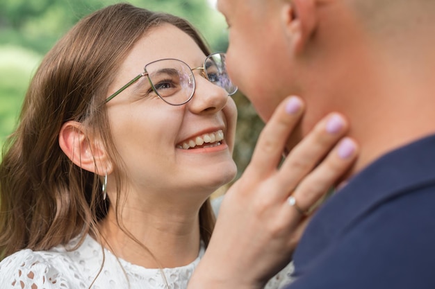 Close up portrait of beautiful woman with dark hair in eyeglasses smiling and trying to kiss boyfrie