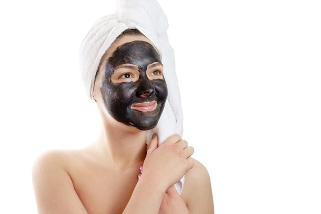 Close-up portrait beautiful woman with facial black mask on white background, girl with a white towel on her head, satisfied and happy  smile