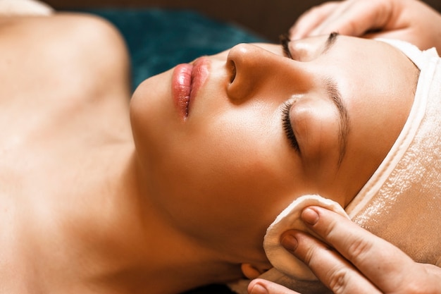 Close up portrait of a beautiful young woman doing a face cleaning before face procedures in a wellness spa center.